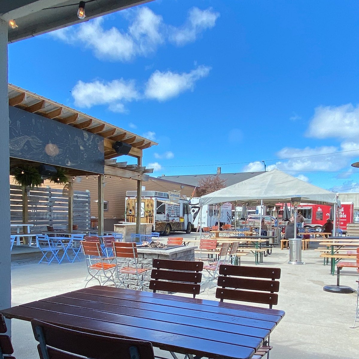 Sunny outdoor patio with food trucks, bistro tables and string lights